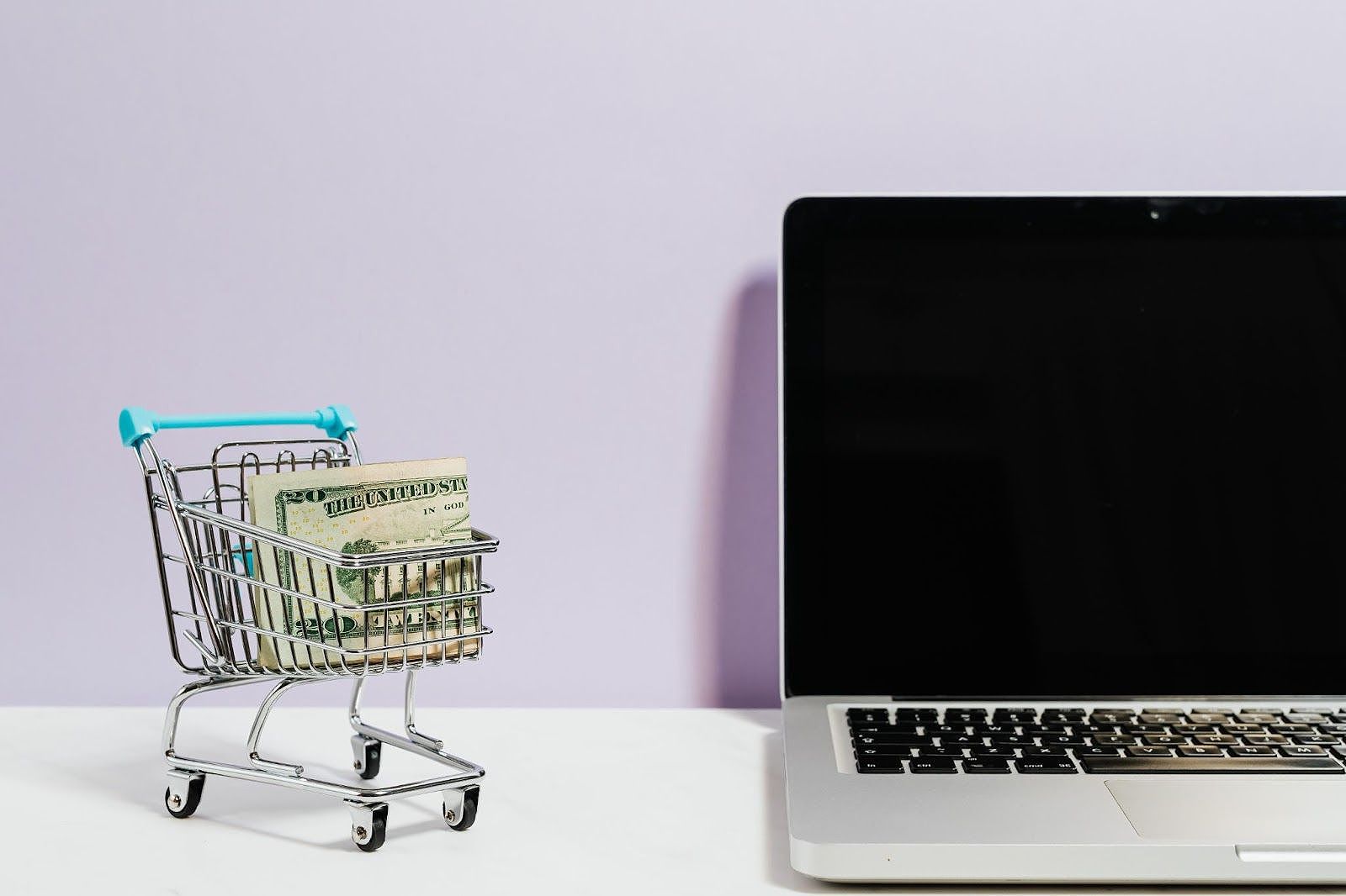 Tiny cart with money next to a laptop